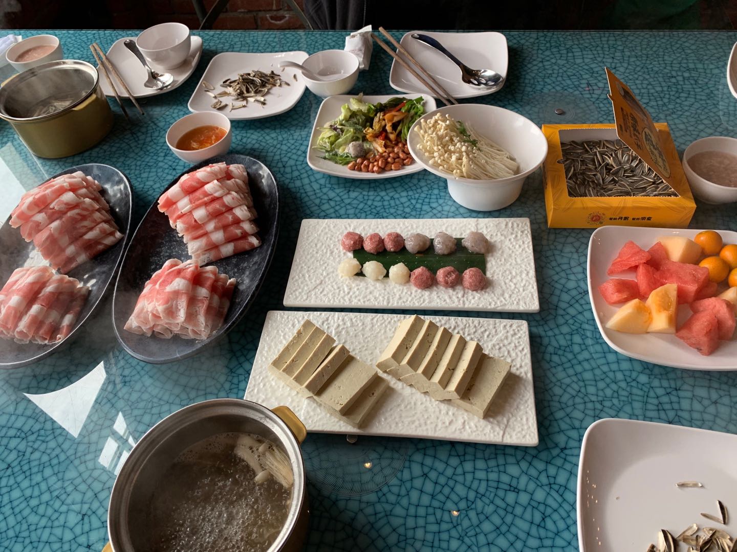 table with plates of raw meat, vegetables, and fruits for hot pot