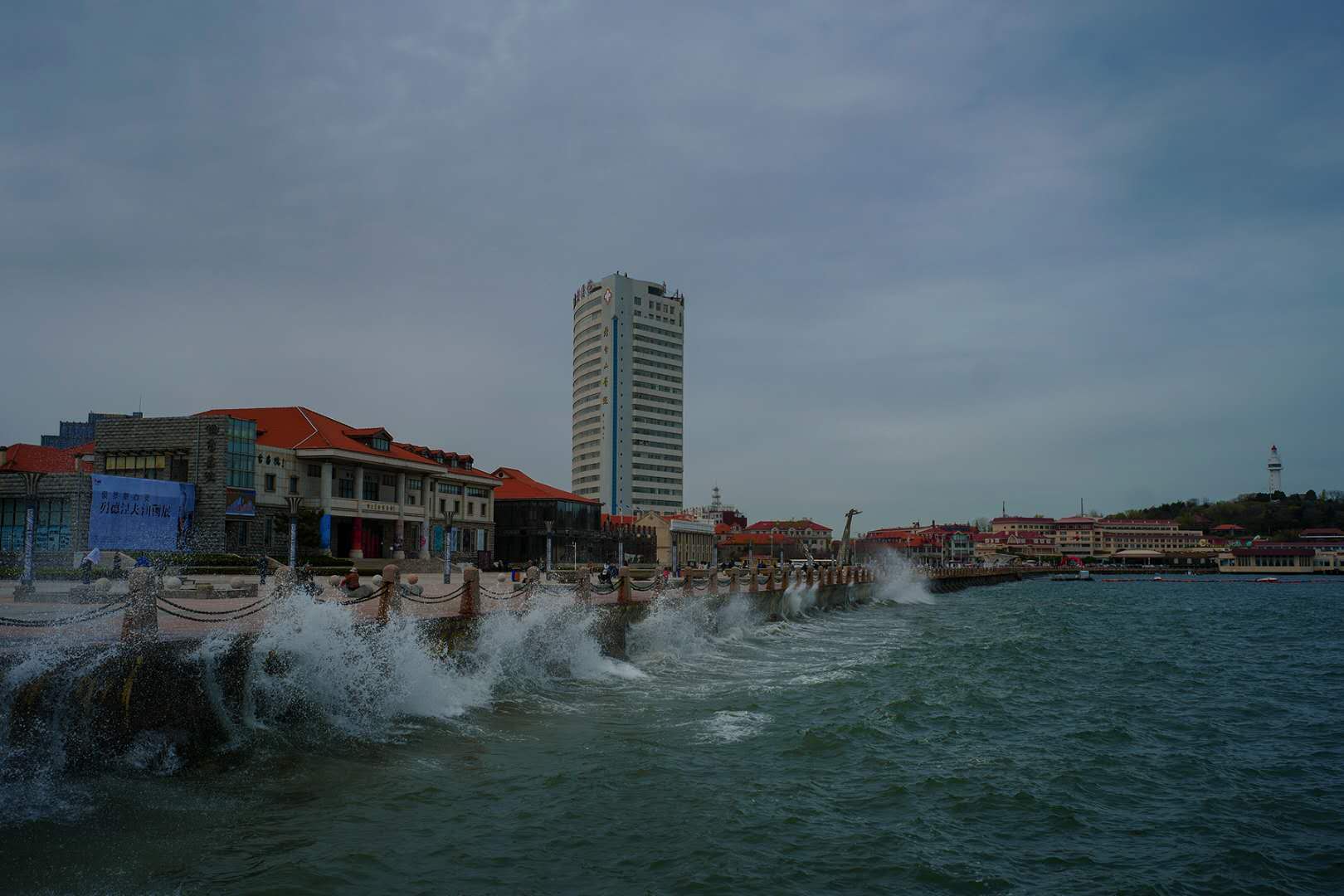 waves crashing on dock with tall building in background